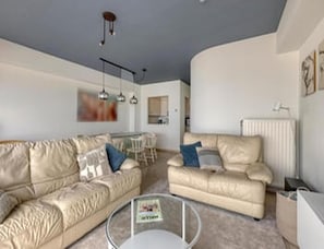 A living room with a sofa, a coffee table, and a dining area with chairs. - Sea View Apartment for 6 in Zeedijk (Blankenberge)