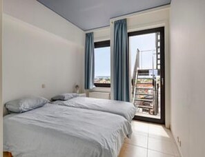 A bedroom with a bed, a window with curtains, and a view of the outside. - Sea View Apartment for 6 in Zeedijk (Blankenberge)