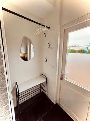 A small, white-walled room with a bench, a mirror, and a door leading outside.