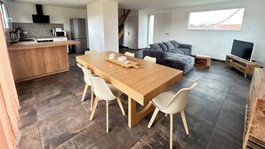 A modern kitchen with a wooden island, a dining area with a wooden table and chairs, a grey sectional sofa, and a TV on a wooden stand. - New 6 person villa with enclosed garden in Ambleteuse (ambleteuse)