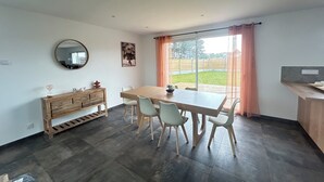 A dining area with a wooden table and chairs, a wooden cabinet, a round mirror, and a view of a backyard through large windows. - New 6 person villa with enclosed garden in Ambleteuse (ambleteuse)