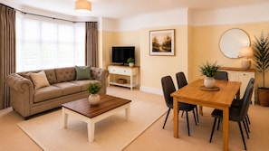 A living room with a sofa, coffee table, TV, dining table, chairs, and a plant. - Beautiful 4 Bed House, Short Walk to Southampton General Hospital, Free parking (Southampton)