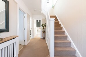 A hallway with a carpeted floor, white walls, and a staircase with beige carpeted steps.