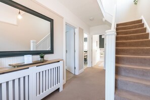 Ein Flur mit Treppe, Heizkörper, Spiegel und einer Tür zu einem anderen Raum.