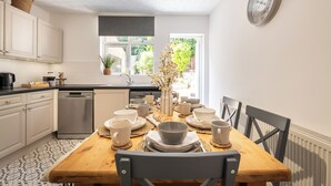 Una cocina moderna con armarios blancos, una mesa de comedor de madera dispuesta con platos, tazas y un florero.
