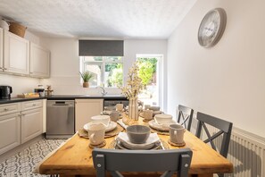 Eine moderne Küche mit weißen Schränken, einem Holzespeisetisch, gedeckten Tellern, Tassen und einem Blumenstrauß.