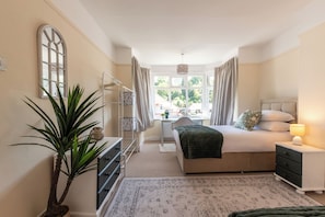 A bedroom with a bed, bedside table, lamp, dresser, and a large window with curtains. - Beautiful 4 Bed House, Short Walk to Southampton General Hospital, Free parking (Southampton)