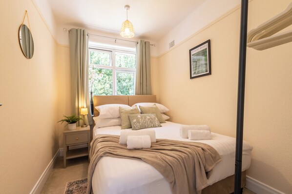 A neatly arranged bedroom with a bed, bedside tables, a lamp, and a window with curtains.
