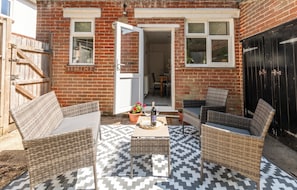 Eine Terrassenfläche mit Korbmöbeln, einem Tisch mit Flasche und Glas sowie einem gemusterten Teppich.