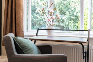 Ett rum med ett fönster, ett element, en stol, ett bord och en vas med blommor.