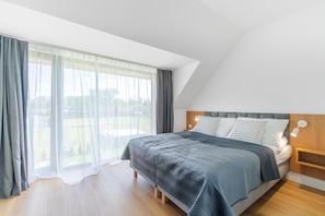 A bedroom with a bed, curtains, a nightstand, and a view of the outdoors. - Comfortable Holiday Home, Dziwnow (Dziwnów)