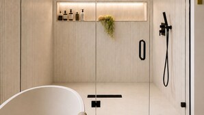 Um banheiro moderno com uma banheira de pedestal, área de chuveiro com box de vidro e nicho embutido com artigos de higiene pessoal.