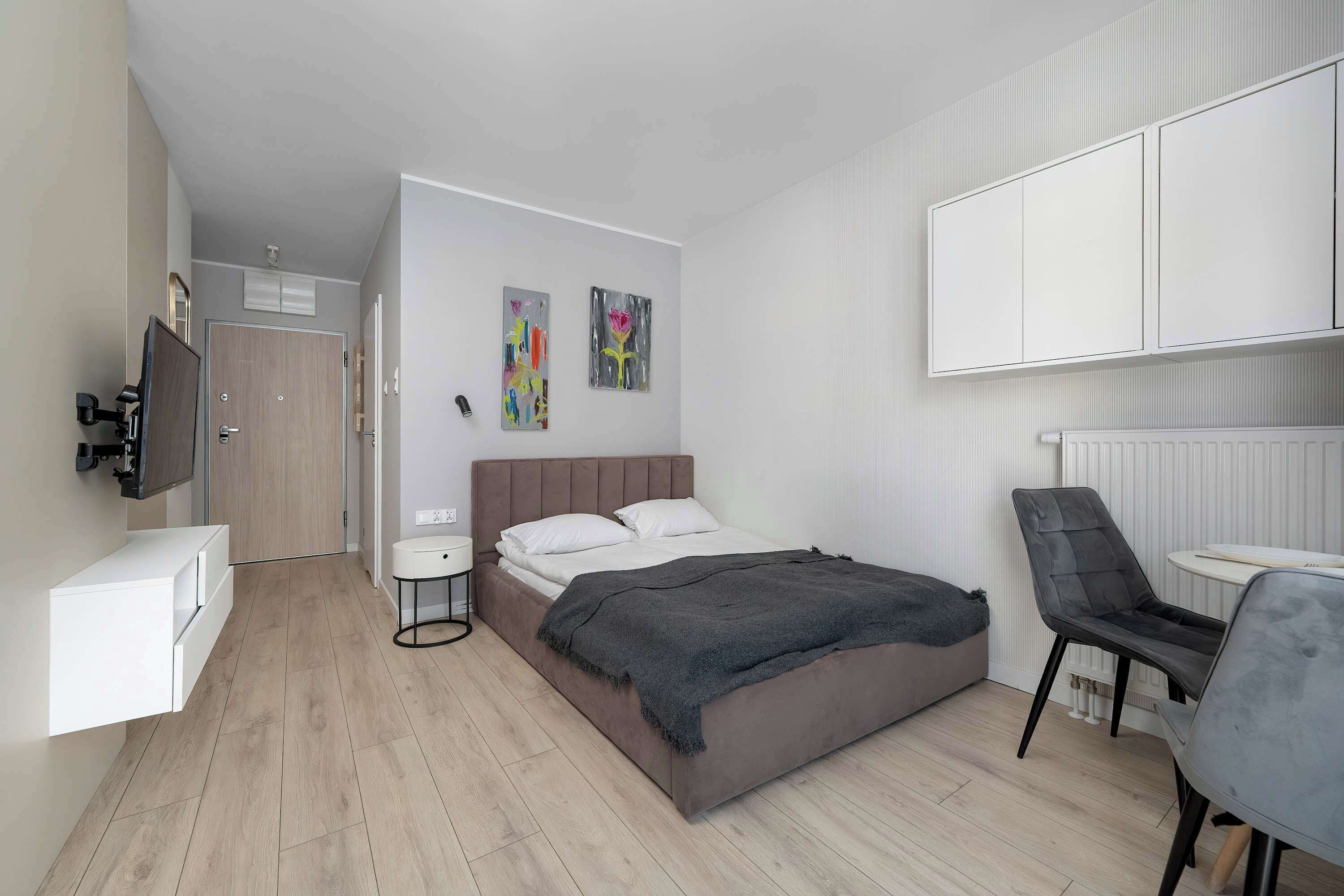 Une chambre à coucher moderne, avec un lit, des tables de chevet, une chaise et des œuvres d’art accrochées au mur.