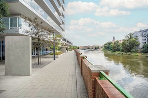 A riverside walkway with a modern building, a brick wall, and a clear sky. - Modern Studio in the City Centre | Close to the High Street (Wrocław)