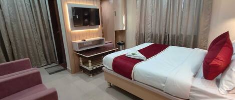 A hotel room with a bed, a TV mounted on the wall, a desk, and a chair.