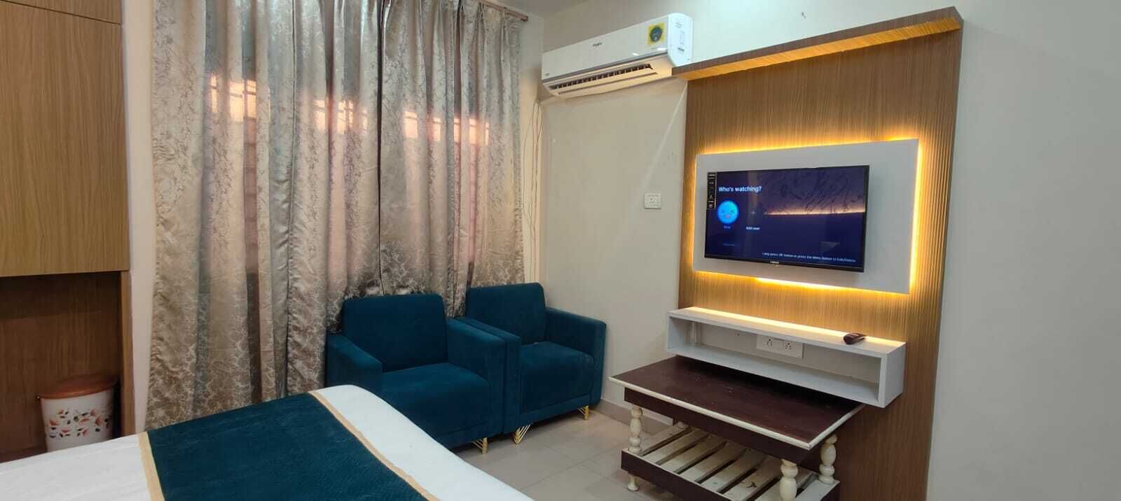 A hotel room with a bed, a TV mounted on a wall, a sofa, and an air conditioning unit.
