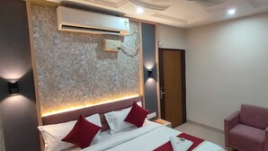 Una habitación de hotel con una cama, una silla roja, un equipo de aire acondicionado y un aplique de pared.
