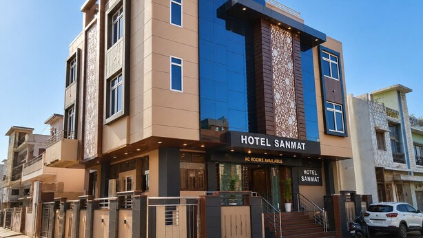 Un hotel moderno con una entrada destacada, un panel decorativo vertical y un cartel que indica disponibilidad de habitaciones con aire acondicionado.