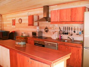 Une cuisine en bois Ă©quipĂ©e dâun four Ă micro-ondes, dâune cuisiniĂšre, dâun Ă©vier et dâustensiles suspendus.
