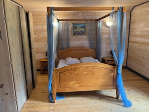 Un lit à baldaquin en bois, une table de chevet, une petite table et un tableau accroché au mur.