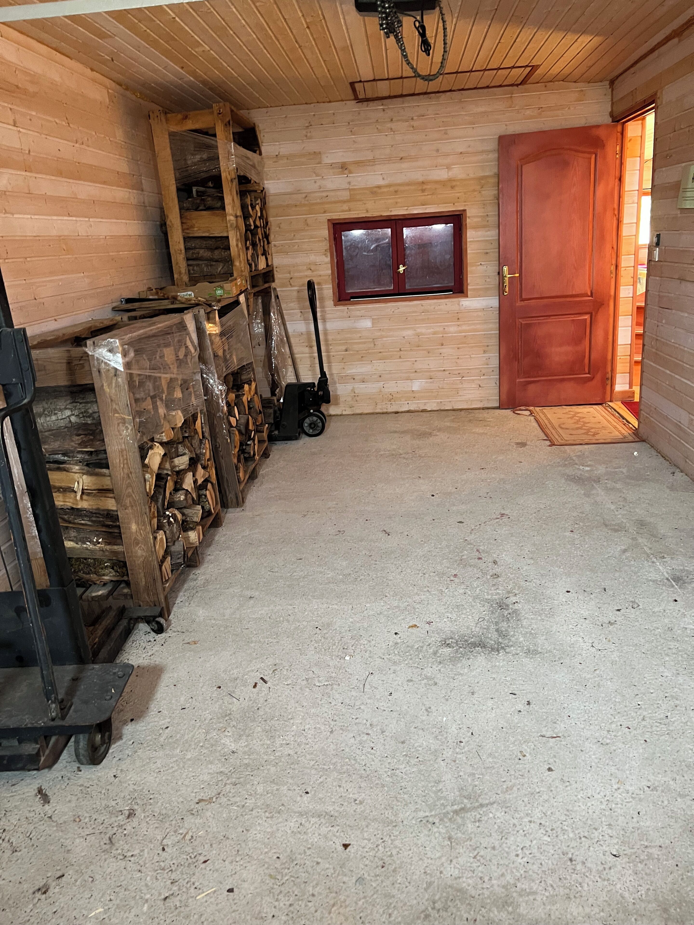 A wooden interior with a door, a window, and a stack of firewood.
