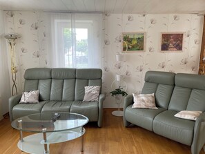 A living room with two green sofas, a glass coffee table, a floor lamp, and floral wallpaper. - Kannemann vacation apartment (Herzberg am Harz)