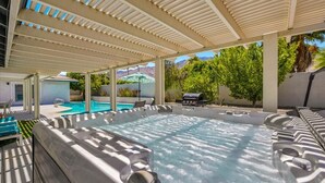 Ett område med ett bubbelbad, en täckt uteplats, en pool och solstolar.
