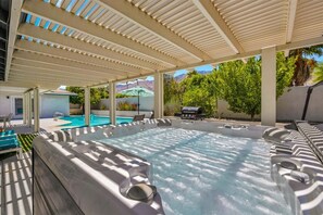 Ein Whirlpoolbereich mit überdachter Terrasse, einem Pool und Liegestühlen.