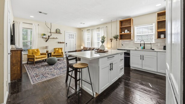 Una cocina amplia con una isla central, taburetes de madera y un comedor con sillas amarillas.