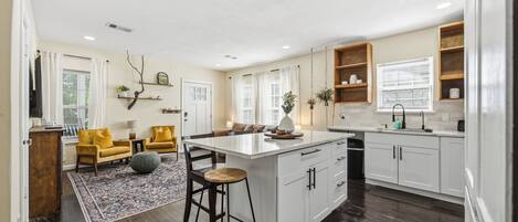 A spacious kitchen with a central island, wooden bar stools, and a dining area with yellow chairs.