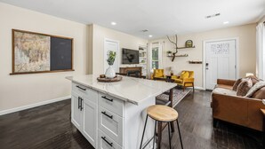 Una cocina moderna con encimera de mármol, un taburete de bar y una zona de comedor con una silla amarilla.
