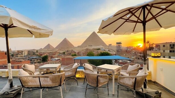 A rooftop terrace with outdoor seating, a view of the pyramids, and a cityscape in the background. - Pyramid-view retreat walk there in minutes (Cairo Governorate)