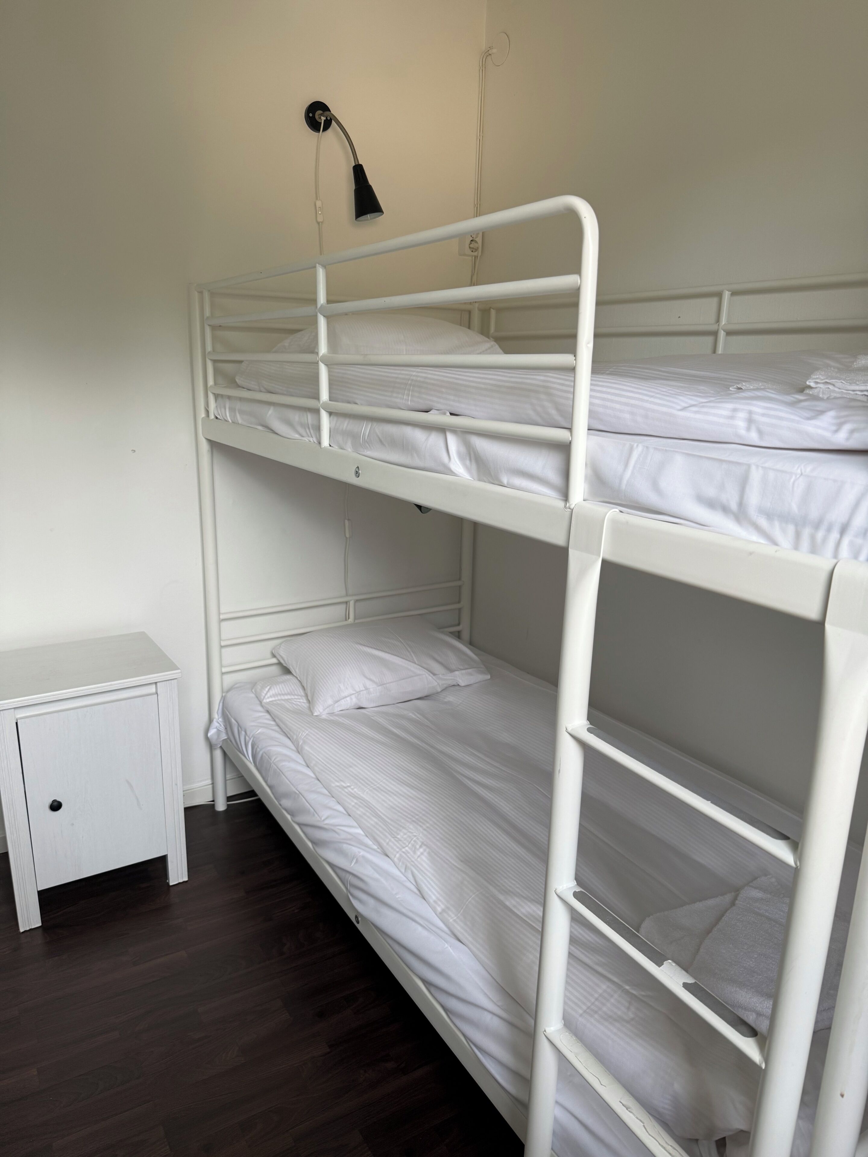 Une chambre avec un lit superposé, une petite table de chevet et une lampe.