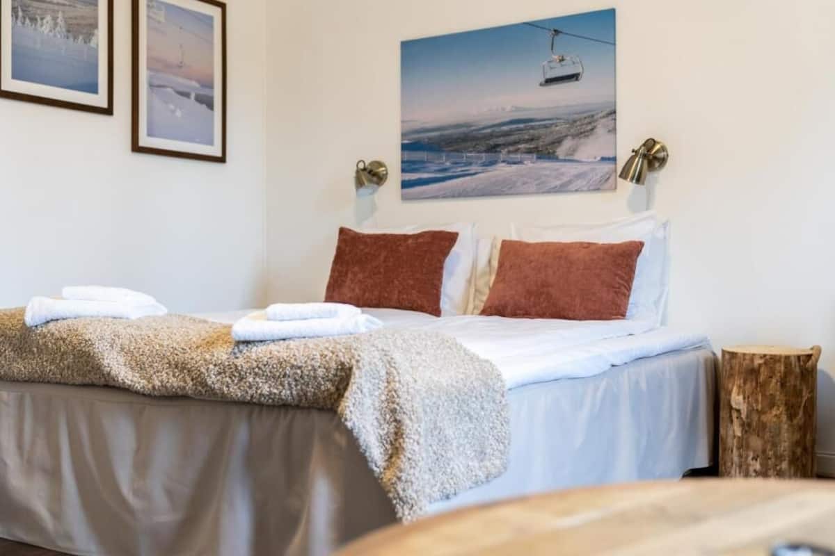 A bed with a fluffy blanket, a wooden nightstand, and a wall-mounted picture of a ski lift.