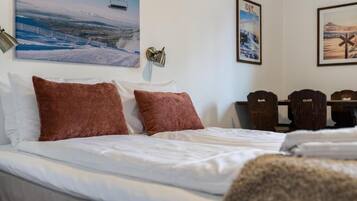 Et hotelværelse med en seng, to brune puder, et hvidt dynebetræk, en vægmonteret lampe, et billede af en skilift og et billede af et bjerglandskab.