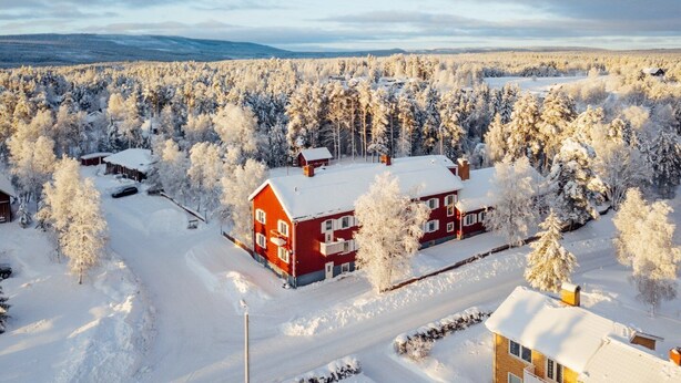 A red building surrounded by snow-covered trees, with a clear view of the surrounding forest. - Hotell Fjällheim (Idre)