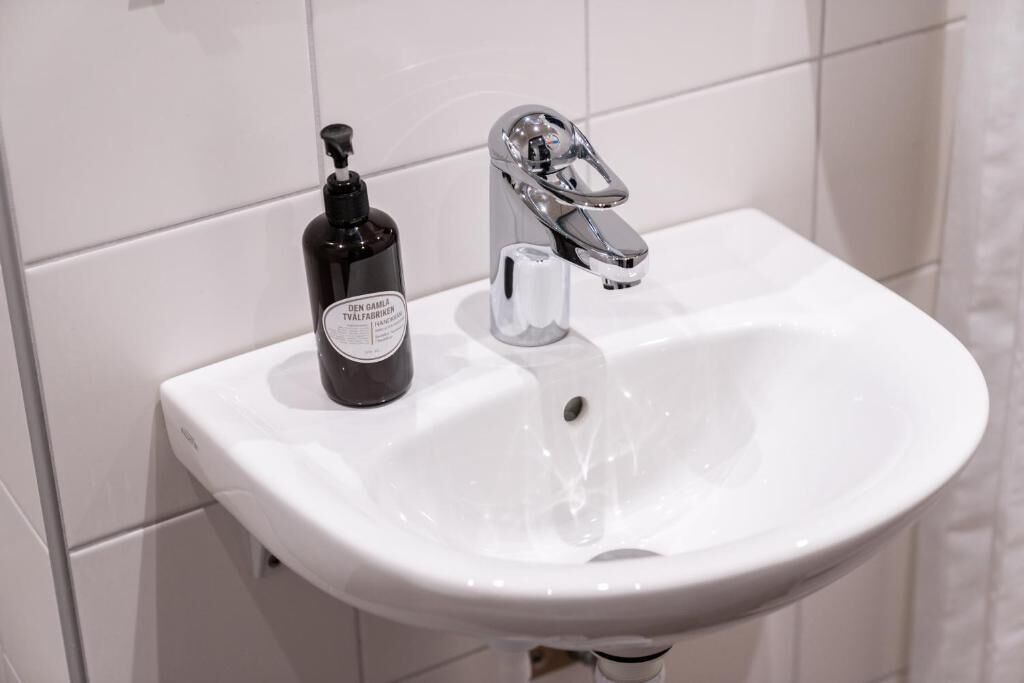 Ein weißes Waschbecken mit einem chromfarbenen Wasserhahn und einer schwarzen Handseifenflasche.