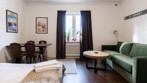 A hotel room with a bed, a green sofa, a round table, a dining table with chairs, a radiator, and a window with curtains. - Hotell Fjällheim (Idre)