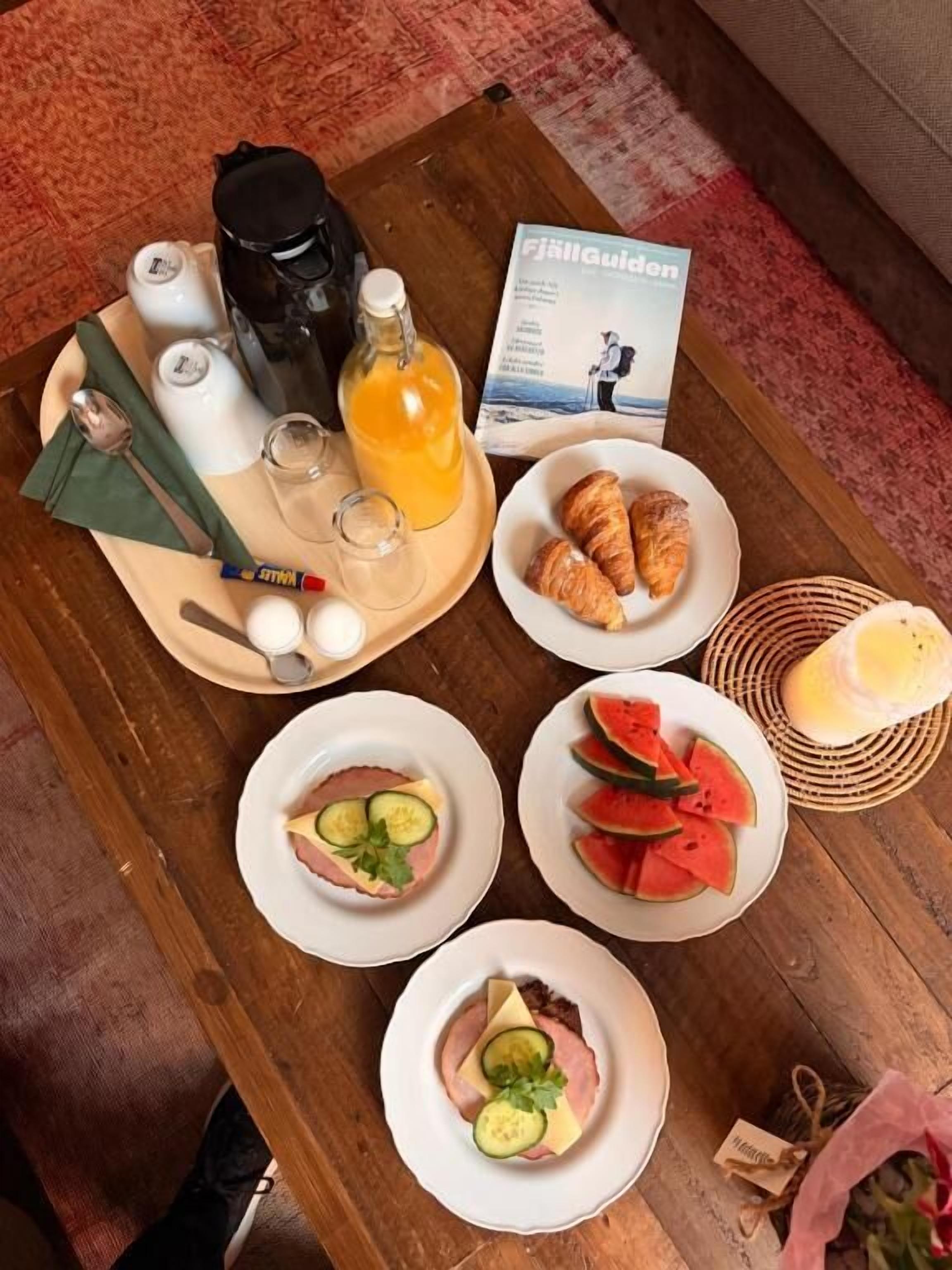 A breakfast buffet with croissants, watermelon slices, ham with cheese, and orange juice.