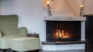 A room with a fireplace, a green armchair, and a small table with a candle. - Hotell Fjällheim (Idre)