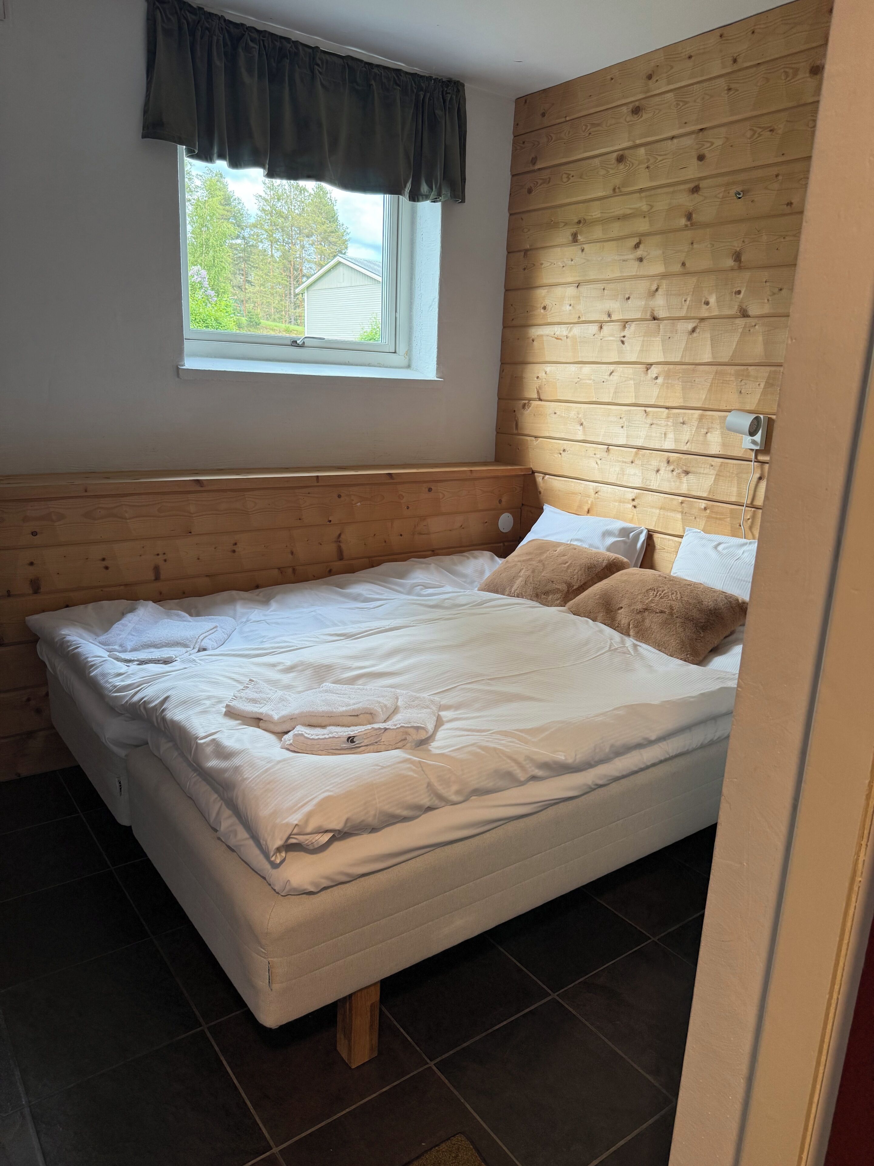 A single bed with white bedding, a window with a dark valance, and a wooden headboard.
