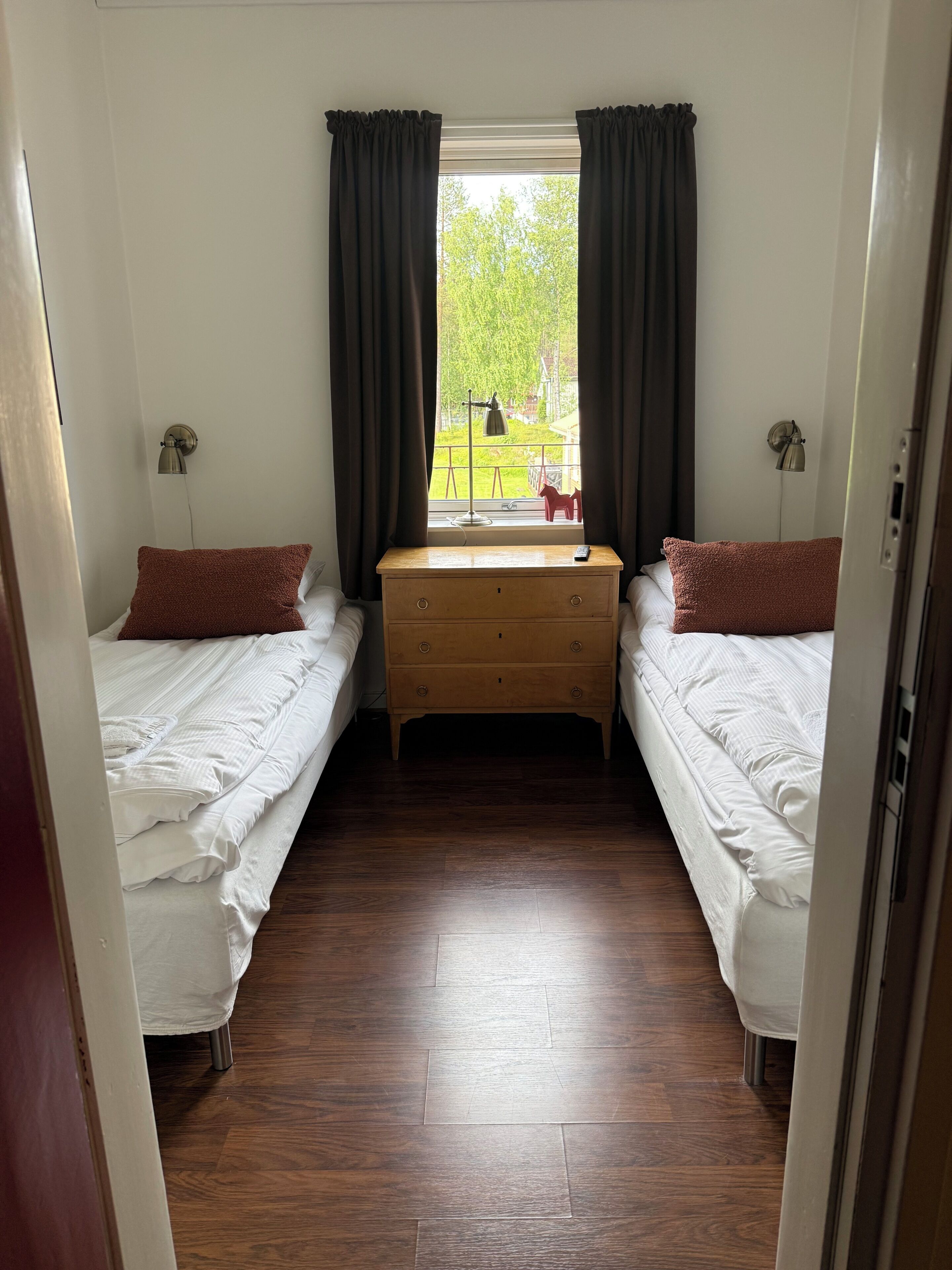 Una habitación con dos camas individuales, un aparador de madera, una ventana con cortinas y vistas al exterior.