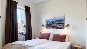 A hotel room with a bed, curtains, a painting, and a nightstand. - Hotell Fjällheim (Idre)