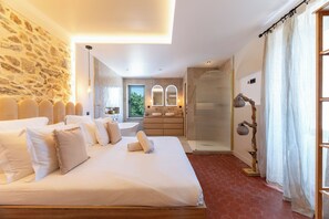 A spacious bedroom with a large bed, a stone wall, a bathroom with a shower, and a view of the outdoors. - VILLA 6 BEDROOMS 7 BATHROOMS WITH SWIMMING POOL Lovely garden with pétanque court. (Sainte-Maxime)