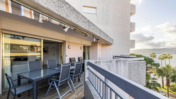 A balcony with a dining table and chairs, a view of the sea, and a building with a stone facade. - Apt With Terrace and sea View, 2min From the Beach (Antibes)