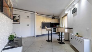 A modern kitchen with white cabinets, a black countertop, and two bar stools. - Apt With Terrace and sea View, 2min From the Beach (Antibes)