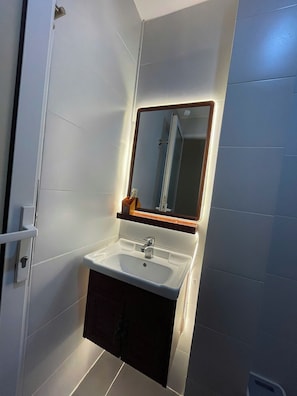 Un baño con lavamanos blanco, un espejo y puerta de ducha.