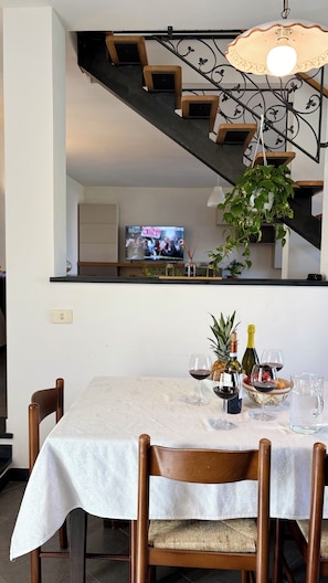 Ein Essbereich mit einem Tisch für zwei Personen, eine Treppe mit dekorativer Geländer und ein Fernseher im Hintergrund.