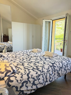 Ein Schlafzimmer mit Bett, Kleiderschrank, Spiegel und einem Balkon mit Blick.