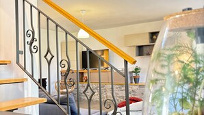 Un escalier avec une rampe en bois, un vase en verre contenant des plantes et, au fond, un mur de pierre.